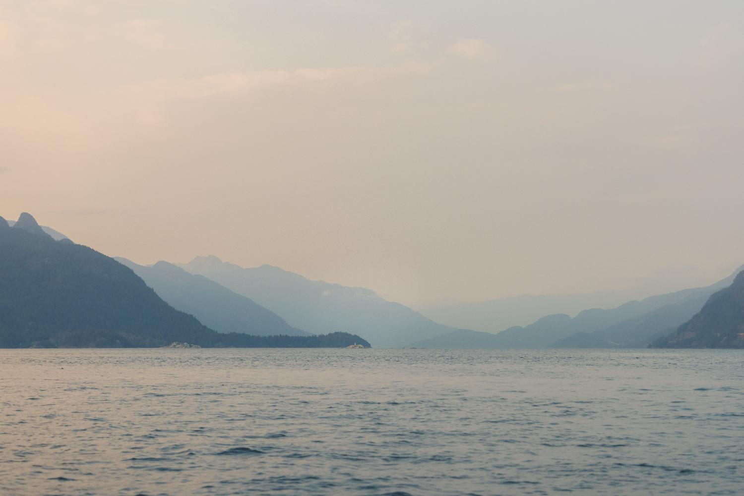 A serene scene of a boat navigating the ocean, framed by towering mountains in the distance.