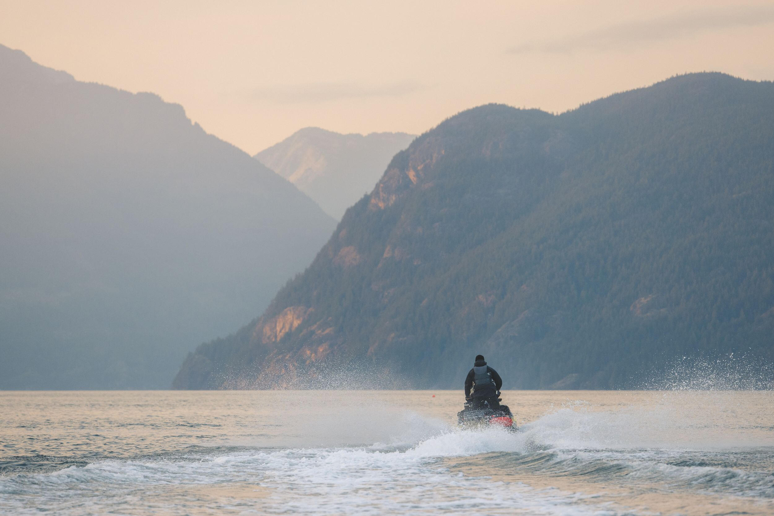 An individual navigates a jet ski through the vibrant ocean, creating splashes against the serene water backdrop.